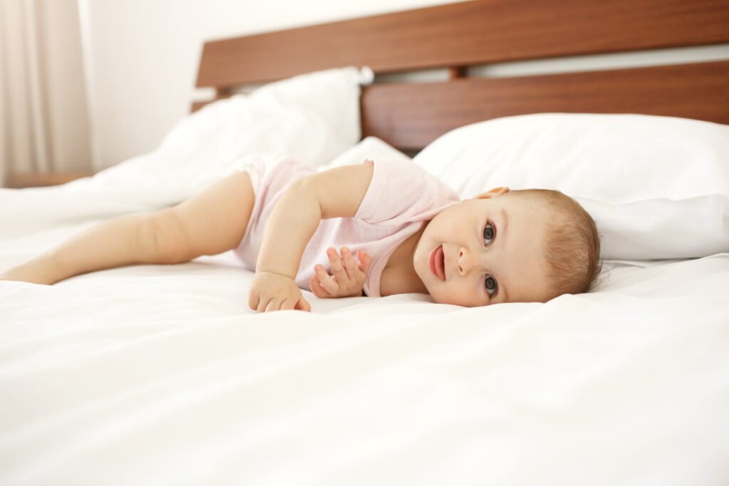 Portrait of beautiful cute newborn baby looking at camera showing tongue lying on bed at home.