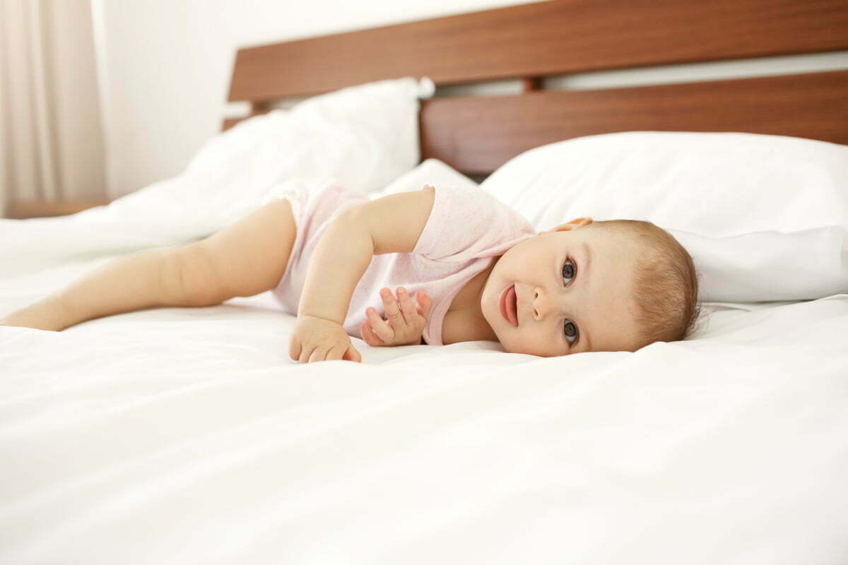 Portrait of beautiful cute newborn baby looking at camera showing tongue lying on bed at home.